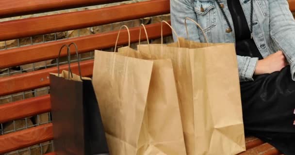 Mujer sentada en el banco y mirando en bolsas de papel de compras — Vídeo de stock