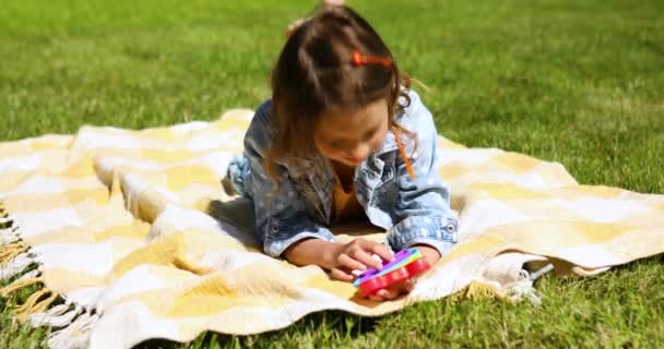 Ragazza si trova su una coperta su erba all'aperto e giocare pop it — Video Stock