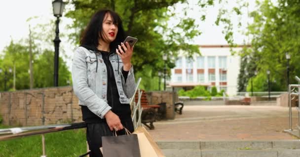 Morena mulher segurando sacos de compras de papel e falando por telefone — Vídeo de Stock