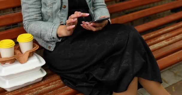 Mujer sentada en el banco del parque con comida para llevar y café — Vídeos de Stock