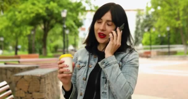 Brunette γυναίκα κρατώντας πάρει μακριά τον καφέ και μιλώντας στο τηλέφωνο — Αρχείο Βίντεο