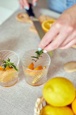 Kadın eli biberiyeyi bardağa, hazırlayan kadın turunçgil ve biberiyeli taze limonatayı evdeki beyaz bir masada, yaz içeceği, sağlıklı su detoksunda yapıyor..