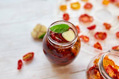 Ev yapımı güneşte kurutulmuş domatesler, beyaz ahşap zemin üzerinde cam bir kavanozda zeytinyağında sarımsak. Üst Manzara. Mutfak için yazdır