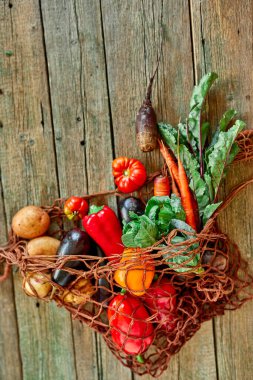 Düz bir çevre dostu ip alışverişi torbası. Taze sebze çeşitleriyle yeniden kullanılabilir ağ torbası. Tahta arka planda biyolojik sağlıklı organik yiyecekler..