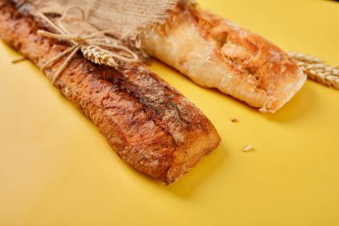 Sarı bir yüzeyde iki baget ekmeğin üst görüntüsü. Ev yapımı ekmek, küçük fırın, doğal tarım ürünleri, yerel gıda, yerli üretim kavramı. Sağlıklı ve lezzetli organik yiyecekler. Boşluğu kopyala.