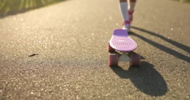 Kaykay kullanmayı öğrenen küçük bir kız, beyaz çoraplar ve pembe ayakkabılar giyen isimsiz bir çocuk yaz şehrinin kırsal kesiminde kaykaya biniyor..