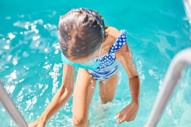 Merdivenlerde gözlüklü bir çocuk havuzdan çıkıyor, küçük bir kız havuzda eğleniyor, evde yaz tatili, tropik tatil beldesi....