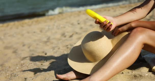 Woman sitting on the sandy beach, putting suncream on her skin — Stock Video