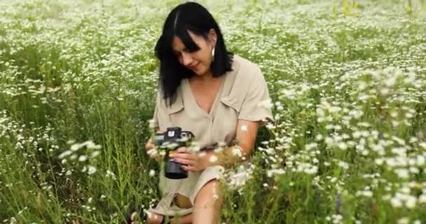 花畑の風景の上に座ってカメラで写真を見ている女性写真家 — ストック動画