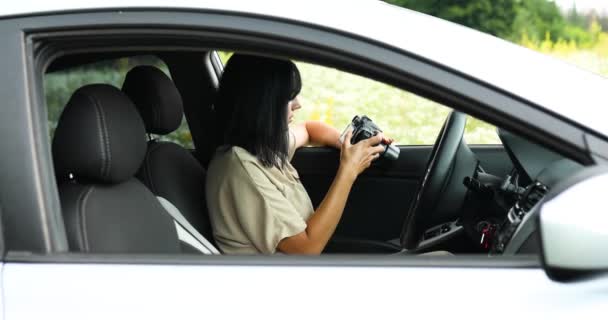 Femme photographe assise dans la voiture et regardant la photo sur l'appareil photo — Video