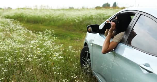 Mujer fotógrafa sentada en el coche y fotografiando un paisaje de campo de flores — Vídeo de stock