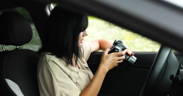 Mulher fotógrafa sentado no carro e olhando para a foto na câmera — Vídeo de Stock