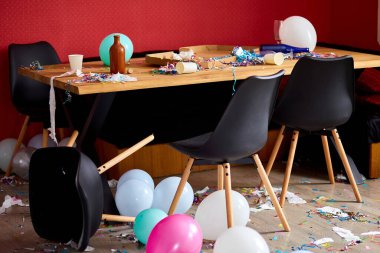 Parti kaosundan sonra, evdeki oturma odasında dağınıklık, pizza ve şampanya bardaklarıyla dolu masa konfeti ve balonlarla kaplı, parti sonrası sabah partiden sonra yerde sandalye..