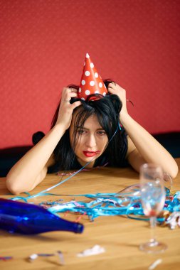 Kırmızı rujlu ve şapkalı genç bir kadın doğum günü partisinden sonra dağınık bir odada yorgun bir şekilde oturuyor.