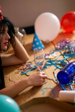 Kırmızı rujlu ve şapkalı genç bir kadın, doğum günü partisinden sonra dağınık bir odada uyuyor, partiden sonra evde yorgun bir kadın.