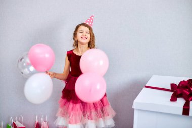 Pembe elbiseli ve şapkalı şirin küçük kız doğum günü partisinde balonlarla oynuyor, mutlu yıllar. Kutlama.