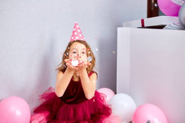 Güzel küçük kız çok renkli konfetileri havaya uçuruyor, evde doğum günü partisinde eğleniyor. Mutlu yıllar çocuğum..