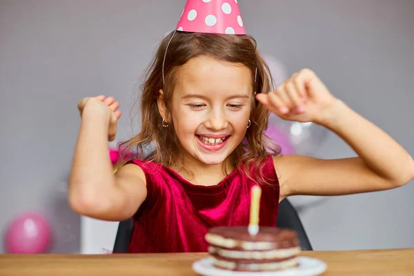 Uśmiech Szczęśliwa Dziewczynka Nosi Kapelusz Urodzinowy Patrząc Tort Urodzinowy Dmuchane — Zdjęcie stockowe