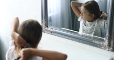 Güzel küçük kız aynanın önünde saçlarını tarıyor.