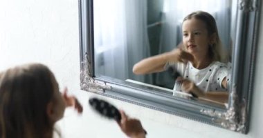 Güzel küçük kız aynanın önünde saçlarını tarıyor.