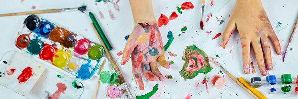 Banner Top view Little girl with painted colorful watercolor hands, child sitting at the table and drawing, Art school concept, girl kid painting at home