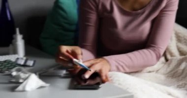 Burnunu silen ve elektronik termometreye bakan hasta kadın, doktoru aramak için telefonu al.