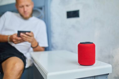 Erkek testi, akıllı telsiz hoparlörü, ses komutlarıyla ev aletlerini kontrol eden adam, evdeki kanepede oturmak, akıllı ev kavramı.