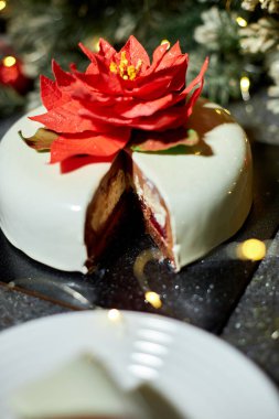 Güzel düzenlenmiş bir tabakta bir dilim bozulmuş pasta, kırmızı kadife ve krem peynir katmanları sergileniyor, yanıp sönen ışıklar ve tatil dekorlarıyla çevrili..