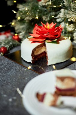Güzel düzenlenmiş bir tabakta bir dilim bozulmuş pasta, kırmızı kadife ve krem peynir katmanları sergileniyor, yanıp sönen ışıklar ve tatil dekorlarıyla çevrili..