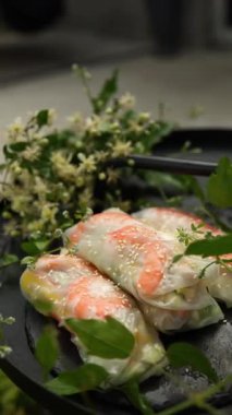 Sebze ve karidesle dolu renkli börekler koyu, yuvarlak bir tepside dizilir. Yemyeşil bitkiler ve narin çiçekler tabağın etrafını sararak canlı bir atmosfer yaratıyor..