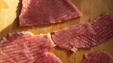 İnce dilimler halinde çiğ et, ahşap bir kesme tahtasının üzerinde pişmeye hazırdı. Mutfakta sıcak ışık var. Yemek hazırlamak için rahat bir ortam yaratıyor..
