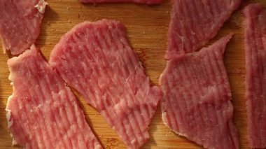 İnce dilimler halinde çiğ et, ahşap bir kesme tahtasının üzerinde pişmeye hazırdı. Mutfakta sıcak ışık var. Yemek hazırlamak için rahat bir ortam yaratıyor..