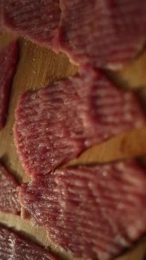 İnce dilimler halinde çiğ et, ahşap bir kesme tahtasının üzerinde pişmeye hazırdı. Mutfakta sıcak ışık var. Yemek hazırlamak için rahat bir ortam yaratıyor..