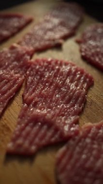 İnce dilimler halinde çiğ et, ahşap bir kesme tahtasının üzerinde pişmeye hazırdı. Mutfakta sıcak ışık var. Yemek hazırlamak için rahat bir ortam yaratıyor..