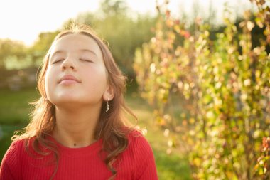 Bir kız kapalı gözlerle bahçede duruyor. Güneş ışığını yüzünde hissediyor. Bitkiler ve ağaçlar onu çevrelemiş. Aydınlık bir gün ve o anın tadını çıkarıyor gibi görünüyor..