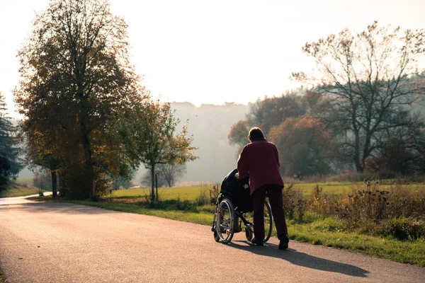 Fogyatékkal élő idősebb ember és asszisztense, a parkban — Stock Fotó