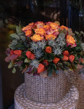 Sarı turuncu güller, filsalis alkekengi, eryngium ametistinum ve sonbahar yapraklarından oluşan güzel bir çiçek aranjmanı Ekim ayında çiçekçide bir vazoda. Dikey. Yakın plan..