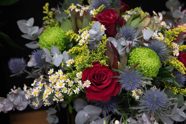 Çiçekçide kırmızı güller, kasımpatılar ve yeşillik olan bir buket. Yatay olarak. Yakın plan..