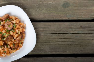 Pişmiş fasulye ve sosis beyaz plaka üzerinde ahşap arka plan kopya alanı ile