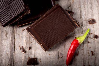 Ahşap arka plan üzerinde kırmızı biber biber kıyılmış çikolata. Ahşap masa makro koyu çikolata çubuğunda kırık parçaları.