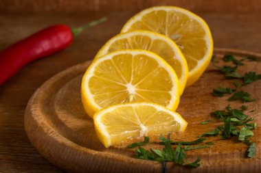 Tahta kesme tahtasında maydanozlu dilimlenmiş limon ve kırmızı acı biber.
