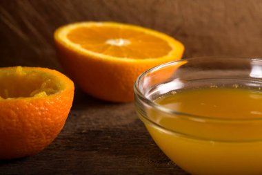 Bir kase taze portakal suyu ve ahşap arka planda yarım portakal suyu.