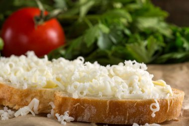 Ekmek tereyağı ve rendelenmiş peynir ve maydanoz arka planda domates dilim