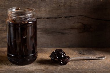 Bir konserve cam ve kaşık eski ahşap rustik arka plan üzerinde kiraz reçeli