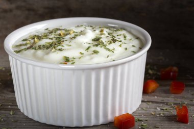 Yoğurttan yapılan sos ve ahşap bir masada seramik bir kasede bulunan otlar.