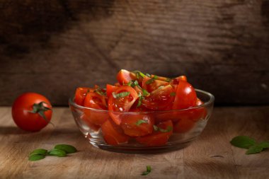 Kiraz domatesinden yapılmış salata ve ahşap arka planda yeşil fesleğen dolu bir kâse.