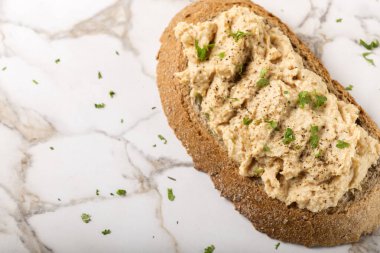 Kremalı ekmek dilimi. Püre tavuk göğsünden yapılmış. Şifalı otlar ve masada karabiber var.