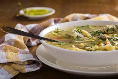 Erişteli tavuk çorbası ve taze sebzeler kaşıkla birlikte beyaz kasede.