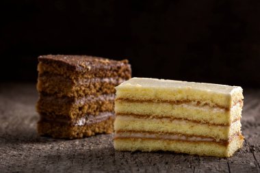 İki dilim pasta, biri kakao kremalı ve diğeri de ahşap arka planda vanilyalı ve peynirli krema.