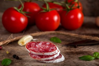İtalyan salamları ahşap üzerinde vişneli domatesler, sarımsak ve otlarla arka planda.